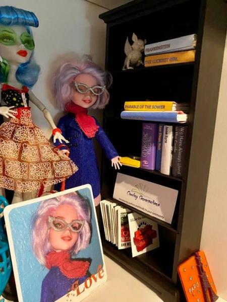 Monster High dolls Ghoulia Yelps and custom Maryelizabeth with pastel pink and blue hair and silver glasses standing next to toy bookshelf with toy gargoyle and doll-sized books on it